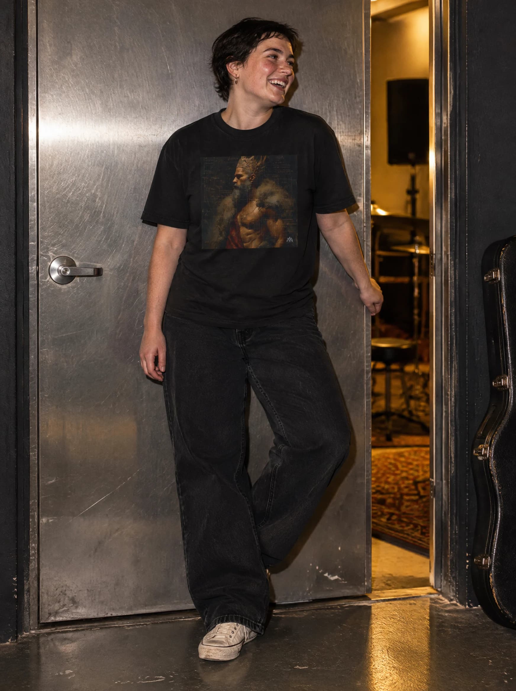 Fictional model laughing beside a steel rehearsal-room door in the black RONIN II tee